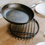 a pan being placed on the steel trivet, sitting on a wooden table. 