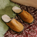 Tan lambskin slippers with cream wool lining resting on a red patterned bedspread