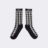 Pair of black and cream houndstooth socks with NOM*d at the cuff, flat lay