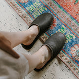 Brown slippers worn on a person, with persian rug. 
