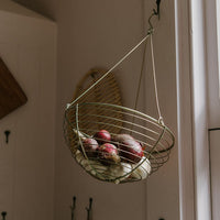 Wire basket hanging in kitchen with onions and garlic in it. 