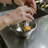 Egg separator in use, with egg yolk caught, over a stainless steel bowl. 