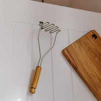 Potato masher and chopping board on hooks on a wall. 