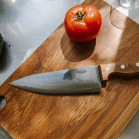Steel knife with wooden handle on chopping board with tomato. 